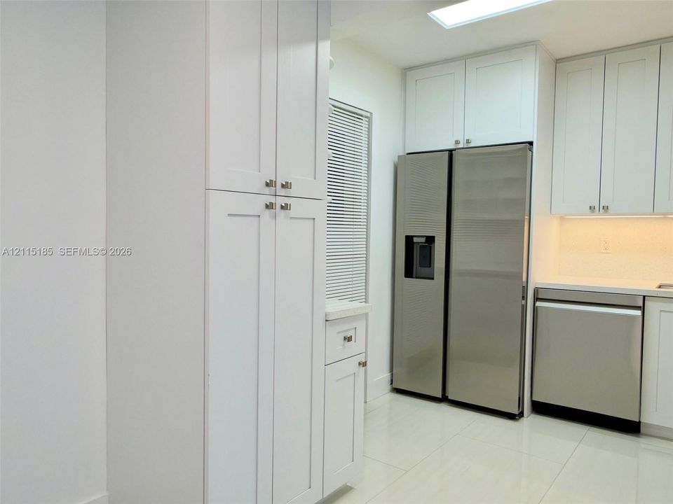 Kitchen featuring white shaker-style cabinetry, stainless steel appliances, polished stone-finish countertops, tile flooring, and a ceiling skylight