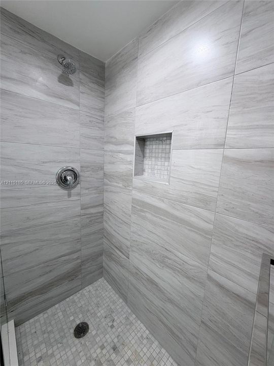 Walk-in shower featuring large-format neutral-toned wall tile, a recessed tiled niche, a mosaic-tiled floor, and a circular shower head with a round control handle