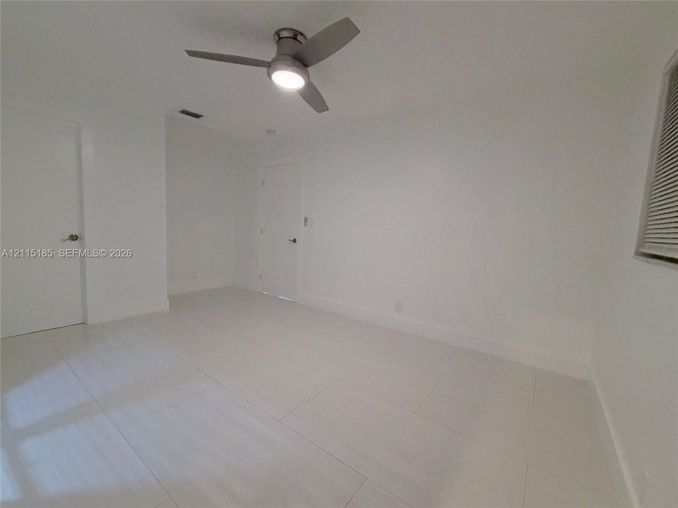 Neutral-toned interior featuring large-format tile flooring, a modern three-blade ceiling fan with integrated lighting, and white interior doors with satin nickel hardware