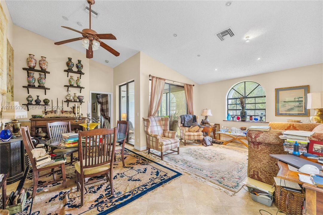 Living area featuring vaulted ceilings, stone-finish tile flooring, recessed lighting, a ceiling fan, and a large arched window