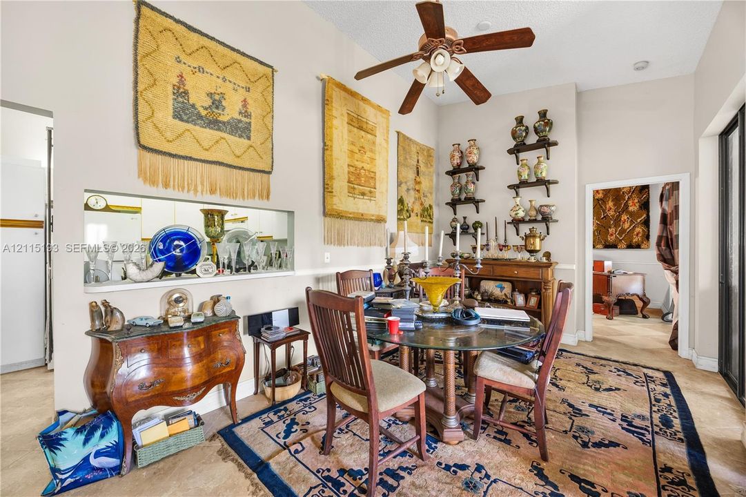 Dining area featuring vaulted ceilings, a central ceiling fan with integrated lighting, and a pass-through window to the kitchen