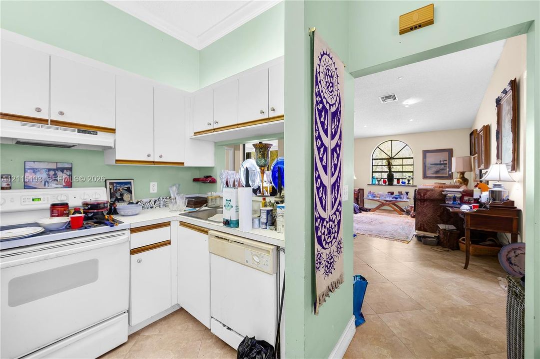 Kitchen featuring white cabinetry, integrated white appliances, and a pass-through opening, with tile flooring visible in the common area
