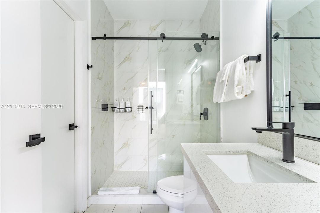 Bathroom featuring a stone-composite countertop, undermount sink, matte black faucet, glass-enclosed shower with sliding barn-style door, and large-format wall tile