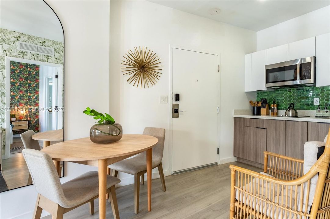 Kitchen featuring wood-finish lower cabinetry, white upper cabinetry, integrated stainless steel microwave, and green glass tile backsplash, accented by wood-finish flooring and a full-length arched wall mirror