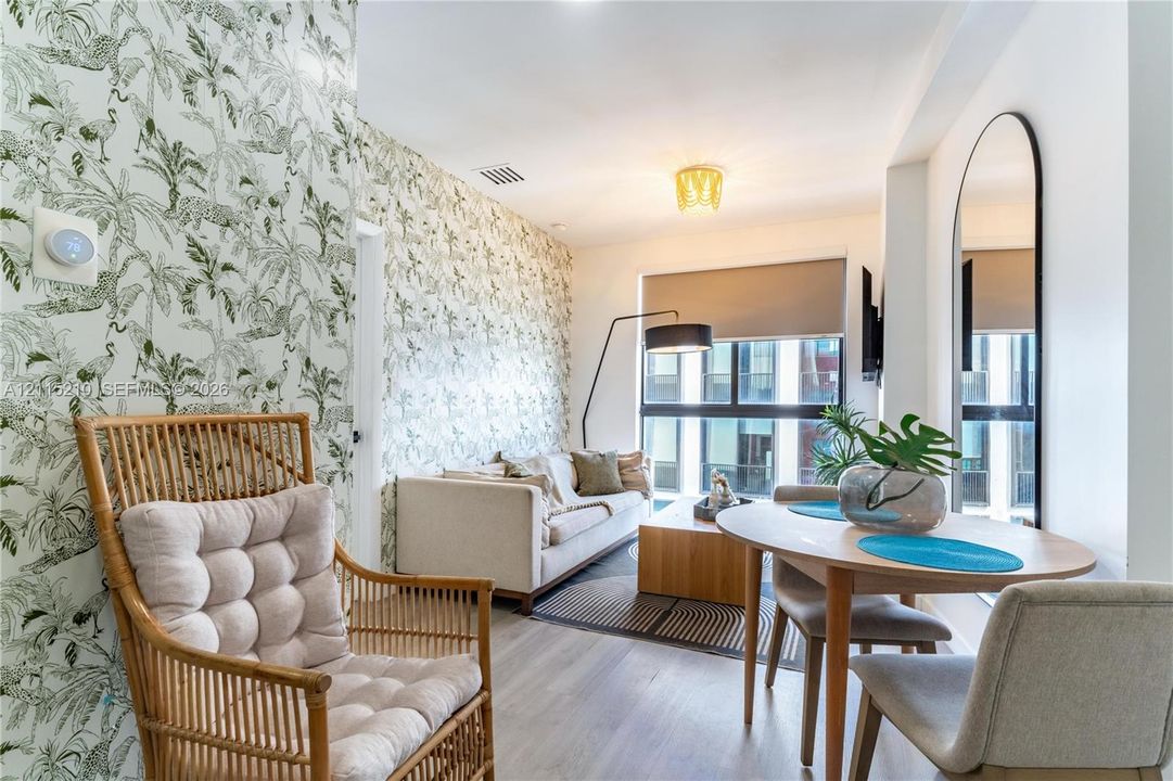 Patterned botanical wallpaper, wood-finish flooring, floor-to-ceiling windows with roller shades, a flush-mount geometric ceiling light fixture, and an arched wall-mounted mirror