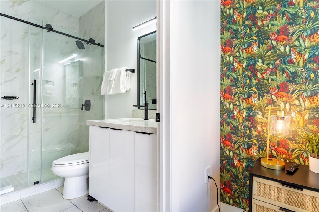 Bathroom featuring a glass-enclosed shower with sliding hardware, stone-finish countertop, white cabinetry, matte black fixtures, and large-format tile flooring