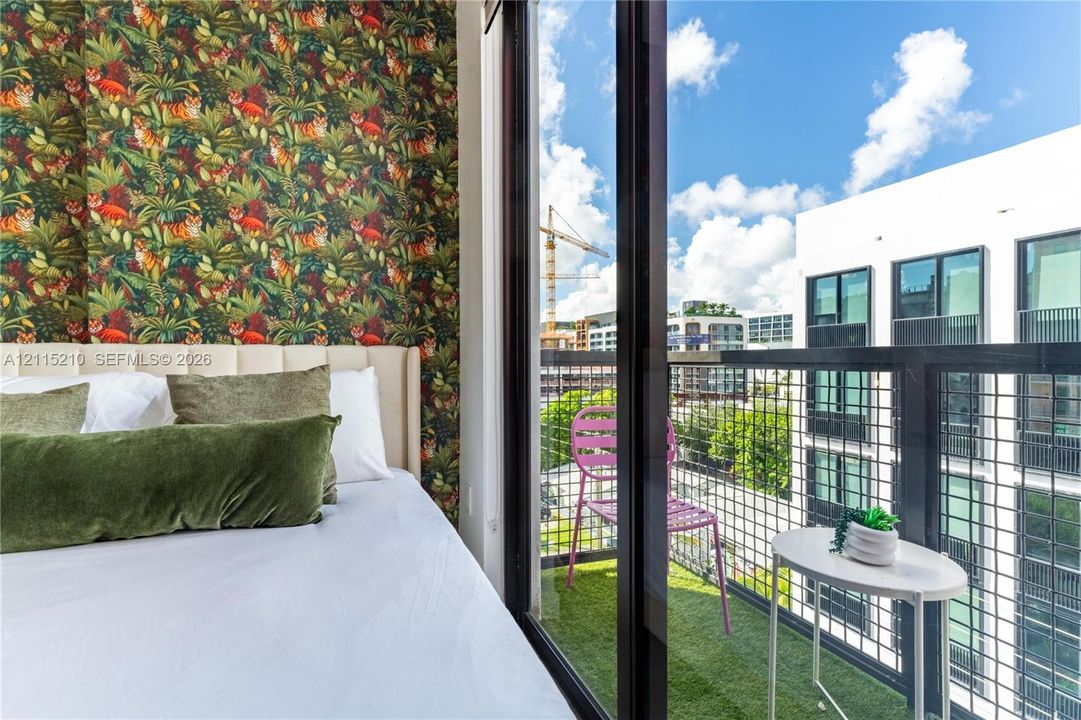 Full-height sliding glass doors opening to a private balcony with metal grid railing and synthetic turf flooring