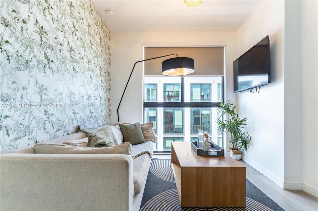 Floor-to-ceiling windows with roller shades, patterned accent wall, and wood-finish flooring
