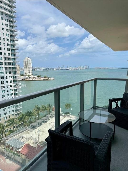 Covered private balcony featuring glass panel railings and tiled flooring, providing expansive water and city skyline scenery