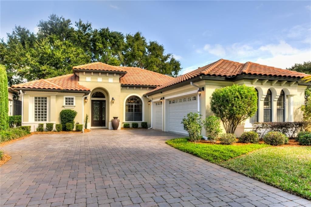 Lovely Spanish Mediterranean style home with paver driveway, lush landscaped yard & architectural multi dimensional tile roof.