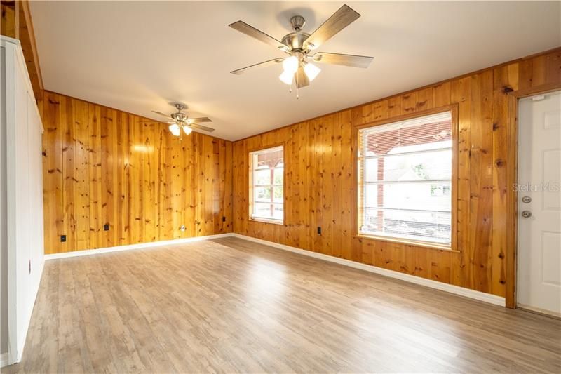 Wood paneled living room with double ceiling fans and new laminate flooring throughout