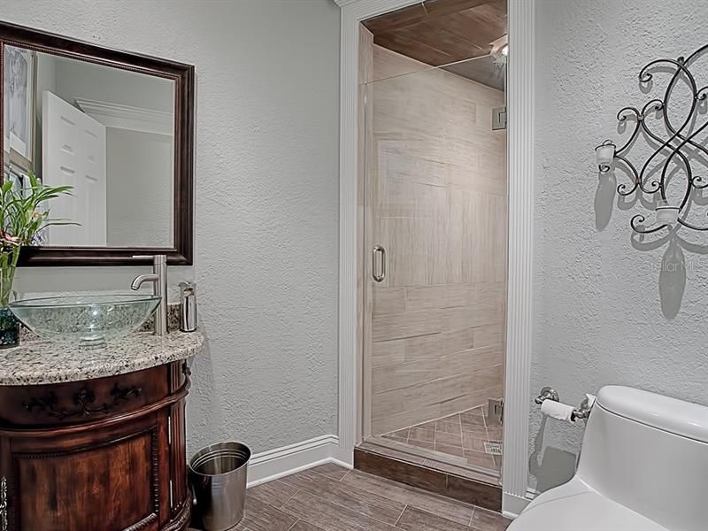 First floor full bathroom features framed mirror, granite counter top, vanity, and vessel sink! The tiled walk-in shower has a frameless glass shower door.