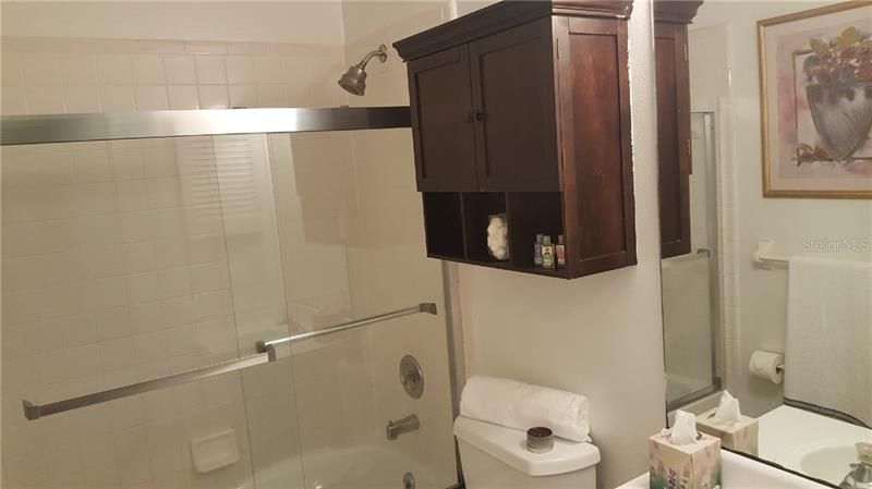 Bathroom 2 has tub and shower combo with sliding clear doors plus built-in shelving, medicine cabinet, and ceramic tile flooring.