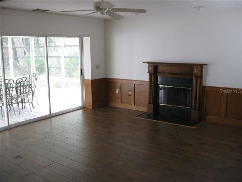 Living Room showing wood burning fireplace, SGDs to Lanai, ceiling fan and wood look ceramic tile floor.