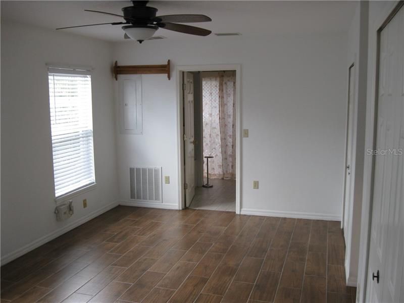 Downstairs Master Bedroom has ceiling fan, wood look tile floor and door in background is to master bath.