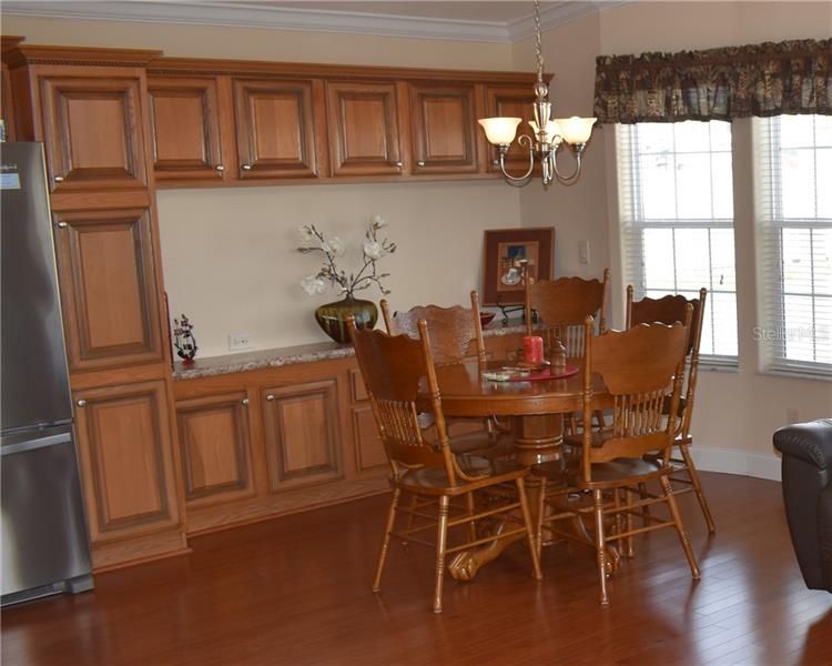View of dining area with pantry next to the SS refrigerator, extra cabinets for storage & engineered hardwood flooring.