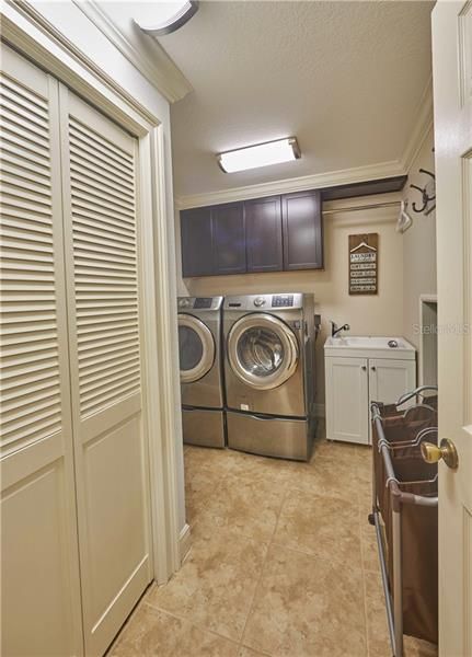 Spacious interior laundry room with sink, real wood cabinets, huge storage closet and spacious storage area under stairs.