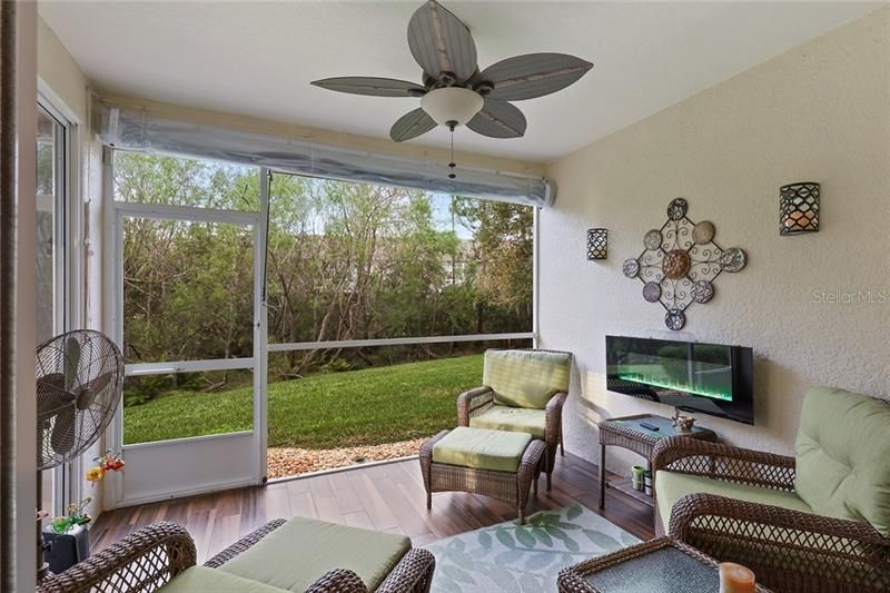 Covered lanai with view of the greenbelt for a quiet private relaxing environment. Wall mounted pebble stone fireplace/heater with colored lights add to the ambiance of this outdoor retreat. Wood tile flooring and clear heavy plastic roll-down shade insulates this room on cold days or nights while still providing a fabulous view of the plush outdoor environment.