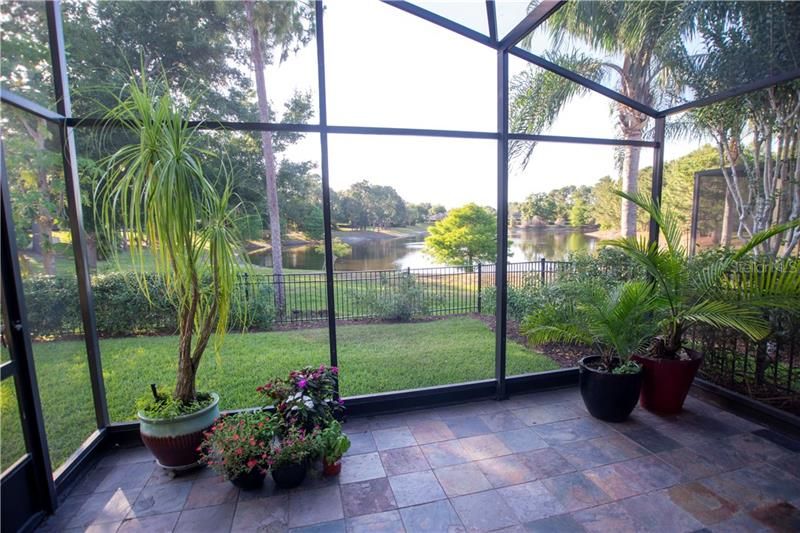 Screened lanai with slate tiles with stunning view of fully fenced back yard and lake.