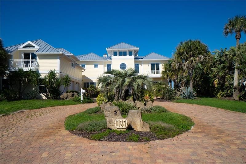 Exterior Key West architecture, spectacular ocean view,  metal roof, non drive side of Ormond Beach, 3 car detached side entry garage with apartment above, circular driveway, coastal palm vegetation.