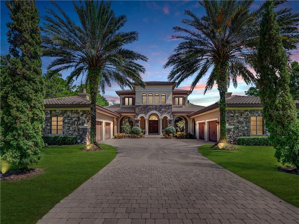 Beautiful front exterior with European flair reflected in its barrel tile roof, wooden doors, stone accents, columns, arched windows, and four car garage.