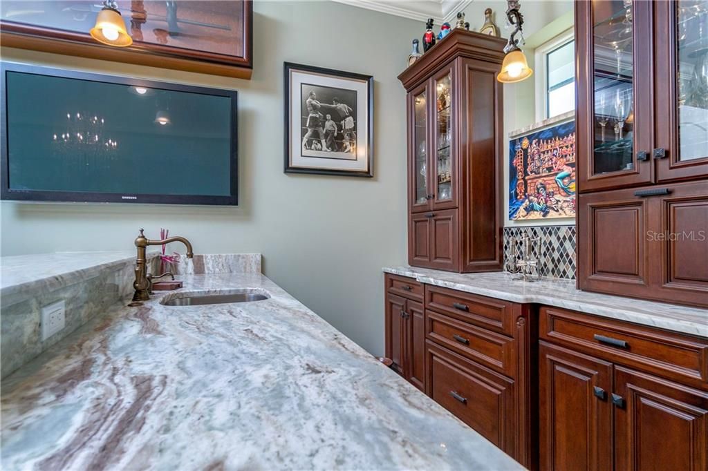 Wet bar has granite counters & tall rich cabinetry that flow from the kitchen. Wine refrigerator built in.