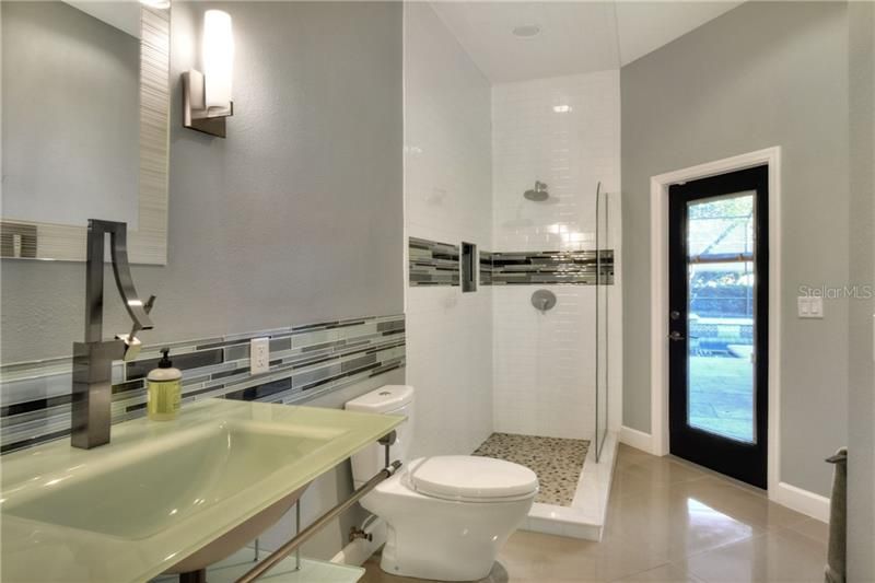 3rd Bathroom that opens to the pool.  Wall mounted sink and open shower with glass door.  Porcelain tile floor.
