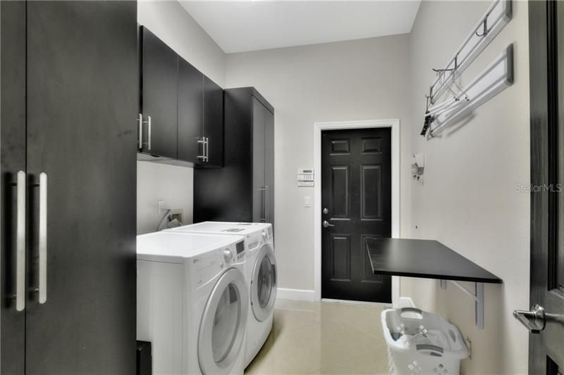 Laundry room with built-ins and folding table. Porcelain tile floor.  Opens to 3 car garage.