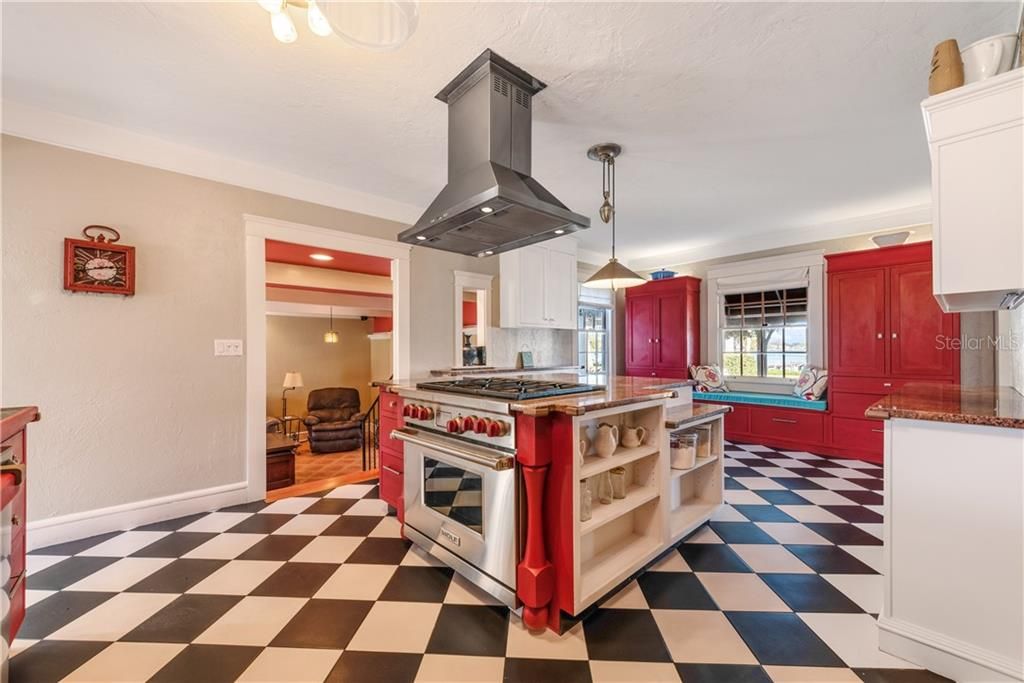 GOURMET KITCHEN featuring a 6 BURNER COOKING RANGE, ISLAND with a floating hood, open & closed shelving for storage, STAINLESS STEEL Appliances, TILED Counters & TILED BACKSPLASH!