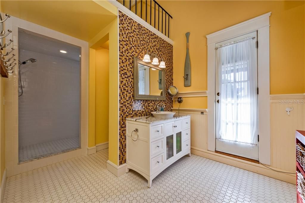 The PRIMARY EN-SUITE BATHROOM offers more WAINSCOTTING, a MARBLE VANITY COUNTERTOP, TILED feature wall, updated light fixtures, WALK-IN SHOWER & Private Balcony Access!