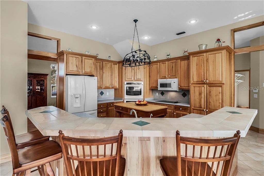 The open kitchen has an oversized breakfast bar, a butcher block free standing island, and Hickory cabinets with a tile backsplash, built-in double ovens and a French door refrigerator.