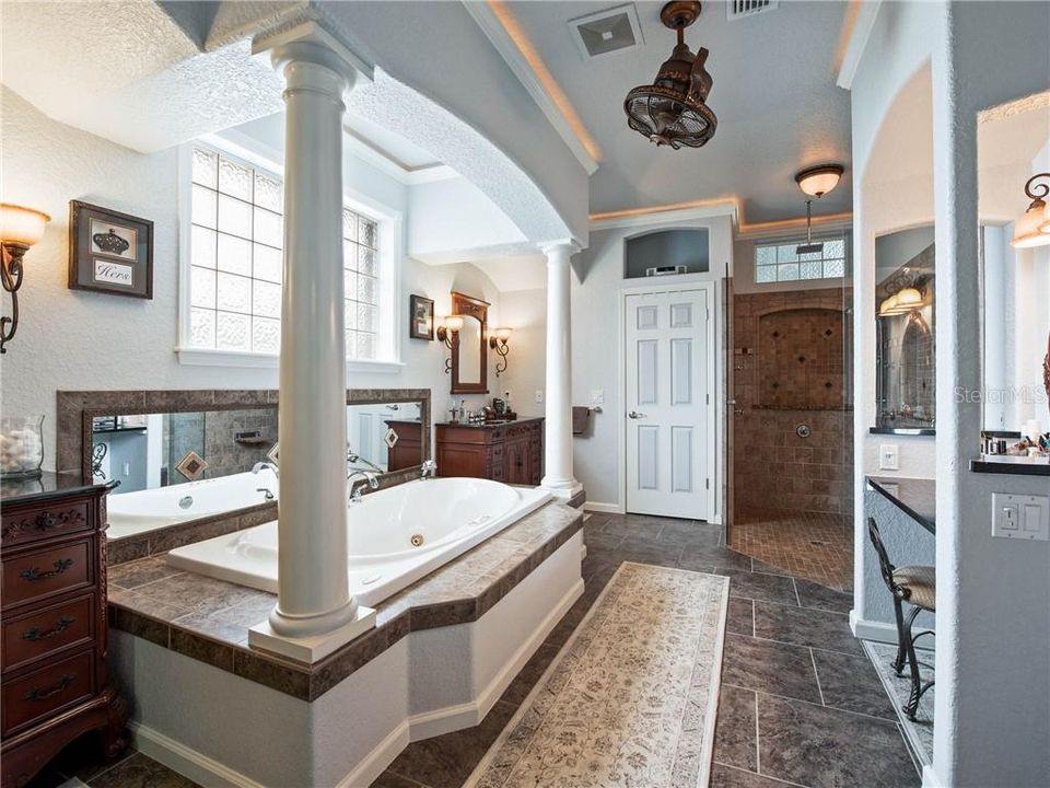 Luxurious Master Bath with the sunken Jacuzzi jetted tub surrounded by columns and rich detail. Notice the lovely shower with frameless glass, His and Her Custom Furniture vanities, and Her very own Dressing and Make up area.