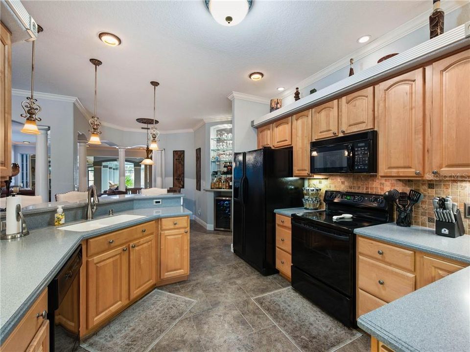 Beautiful Kitchen with staggered ceramic floor tile, arched maple raised cabinetry with brushed nickel hardware, drawer stacks, double trash roll-out, DuPont Corian Countertops with an Integral sink, pull-out faucet, soap dispenser, plant shelf, recess lighting with decorative trim, lovely pendant lights over the bar top, decorative tiled backsplash. View from the Formal Dining looking through the Kitchen into the Breakfast Nook. (Barstools will remain).