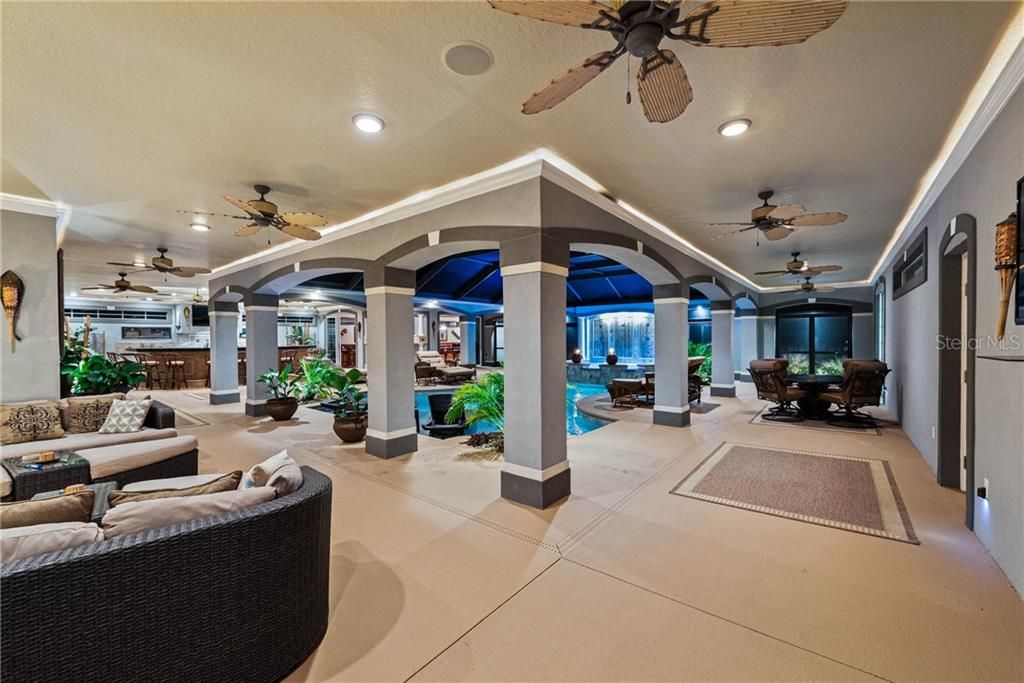 Evening photo of this expansive covered lanai surrounding the pool with several recess lights, ceiling fan and crown molding with ambient rope lighting. This view was taken from the Breezeway door. near the Home Office/In-Law Suite. The spacious Sitting area shown, is right off of the Master Suite.