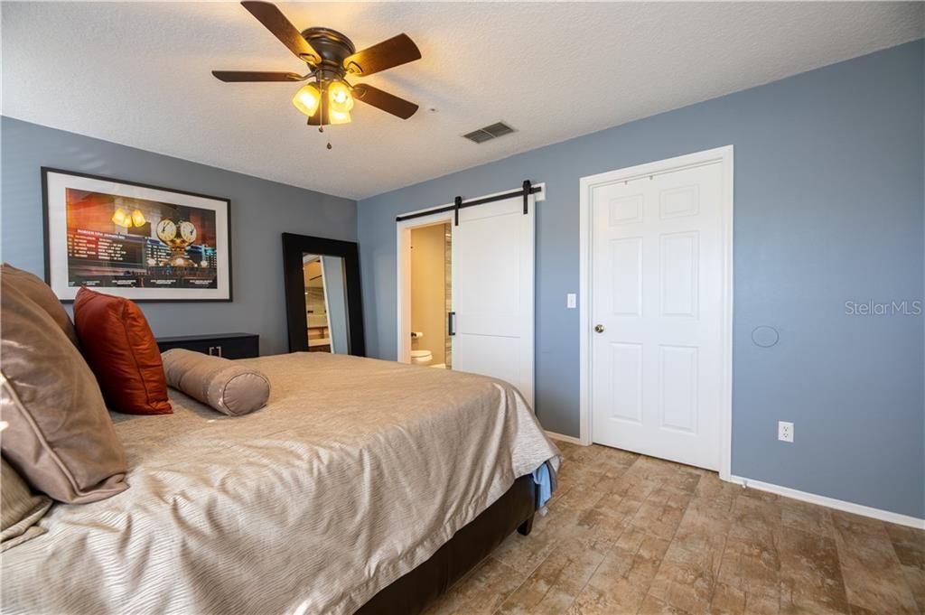 Master bedroom features wood-look ceramic tile flooring and a barn door leads you to master bathroom