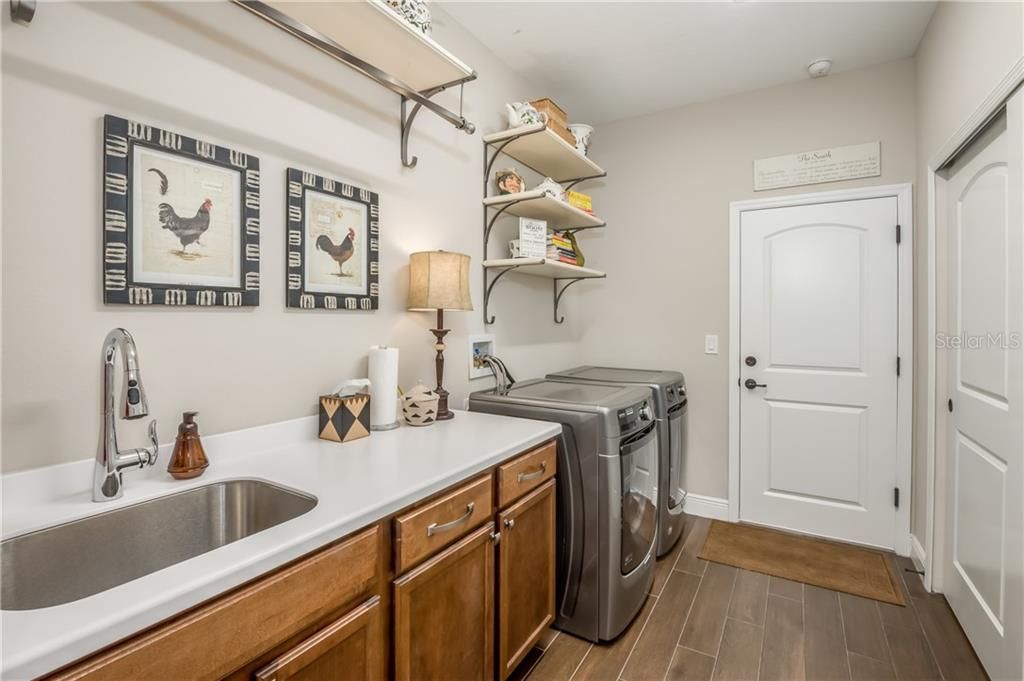 Inside Laundry Room with front load washer & dryer, custom built in pantry, upgraded birch cabinets with deep stainless steel sink and Corian countertops.