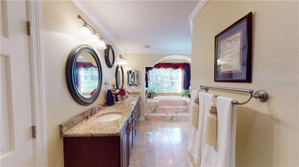 Luxurious master bathroom with oversized walk in shower with multiple shower heads, granite countertops, arch detail, and marble step in soaker tub.