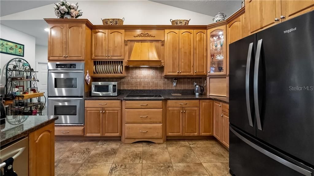 Kitchen with Granite Counters, Tile Backsplash, 42" Custom Cabinets with Crown Molding, Drawer Base, Plate Rack, Glass Doors, Range Hood, Cooktop and Stainless Refrigerator, Double Ovens, Trash Compactor, Microwave