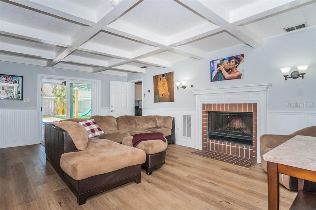 Living room adjacent to kitchen has wood burning fireplace and coffered ceiling.