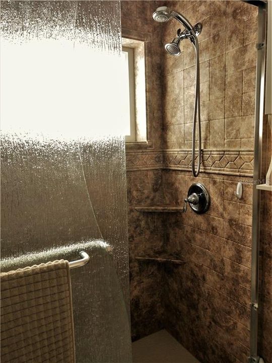 Gorgeous walk in shower features built in shelves, double shower head, large window and sculptured glass shower doors.