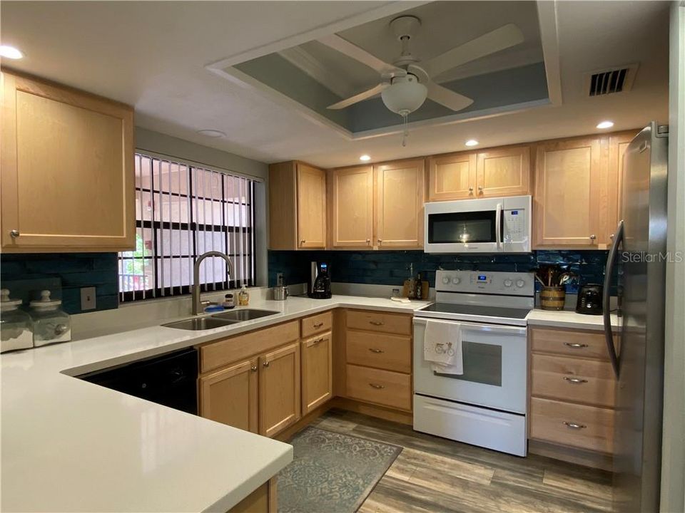 Updated kitchen with wood cabinets, solid surface counters, tile backsplash, kitchen faucet, stainless steel sink, new refrigerator, update can lighting and premium vinyl flooring.