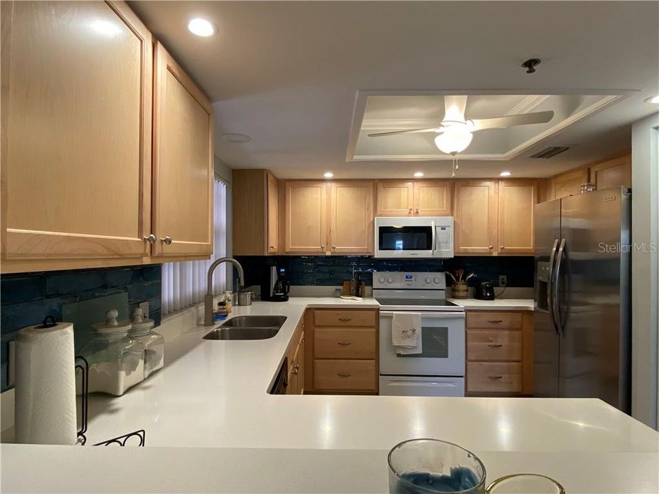 Updated kitchen with wood cabinets, solid surface counters, tile backsplash, kitchen faucet, stainless steel sink, new refrigerator, update can lighting and premium vinyl flooring.