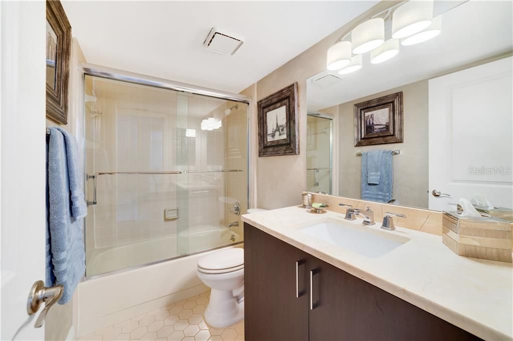 Handicap guest bathroom with enclosed tub featuring marble vanity countertop