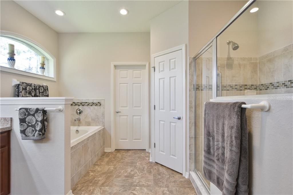 Master bathroom featuring dual vanity, garden tub, separate tiled in shower, large walk in closet, private room for the commode, natural light from an arched window and grab bars.