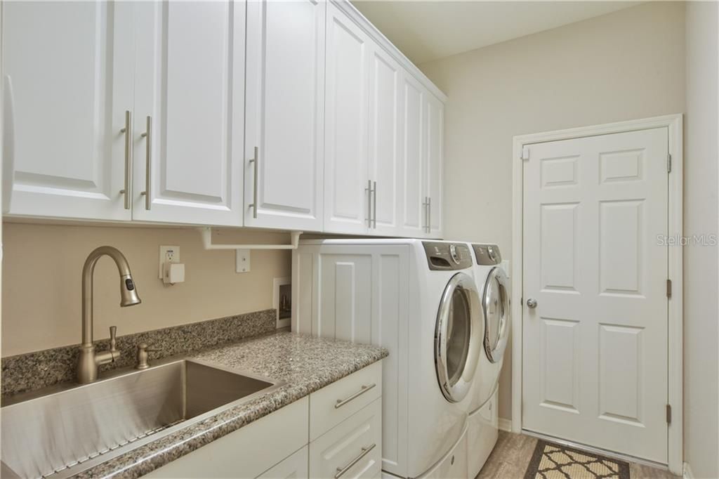 Inside laundry room with large single bowl stainless sink, beautiful white cabinets for additional storage and washer / dryer on pedestals.