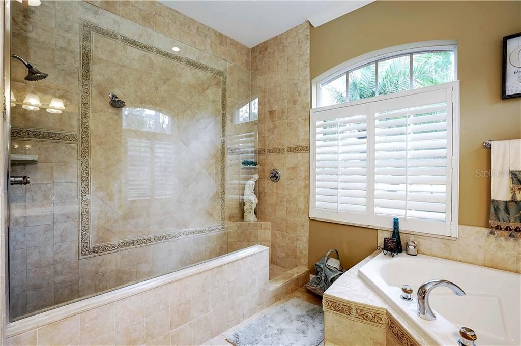 Double shower heads, large shower with detailed tile work and new glass enclosure.