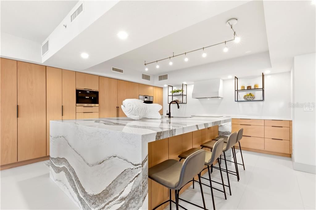 Understated elegance punctuates the designer kitchen.  Wire-brush White Oak cabinetry offer an abundance of storage.  The oversized waterfall island features Cambria quartz and a breakfast bar that is the true centerpiece and heart of the kitchen.