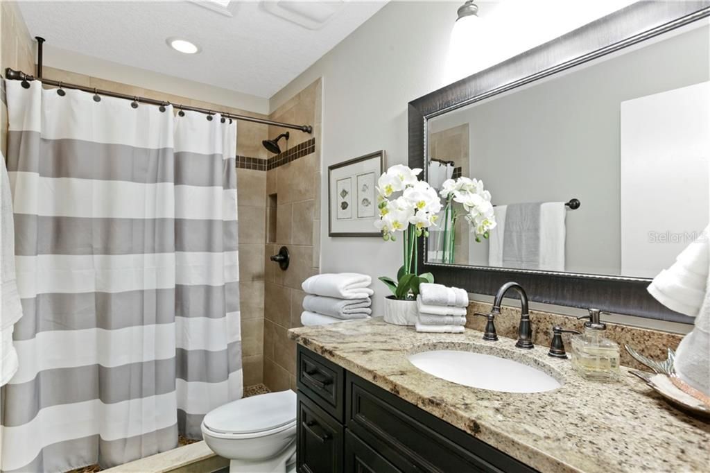 Renovated secondary bath features granite counters and a walk in shower with pebbled floor.
