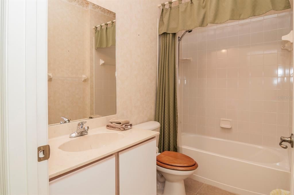 The guest bath has a cultured marble vanity top and a combination tub and shower with a ceramic tile surround.