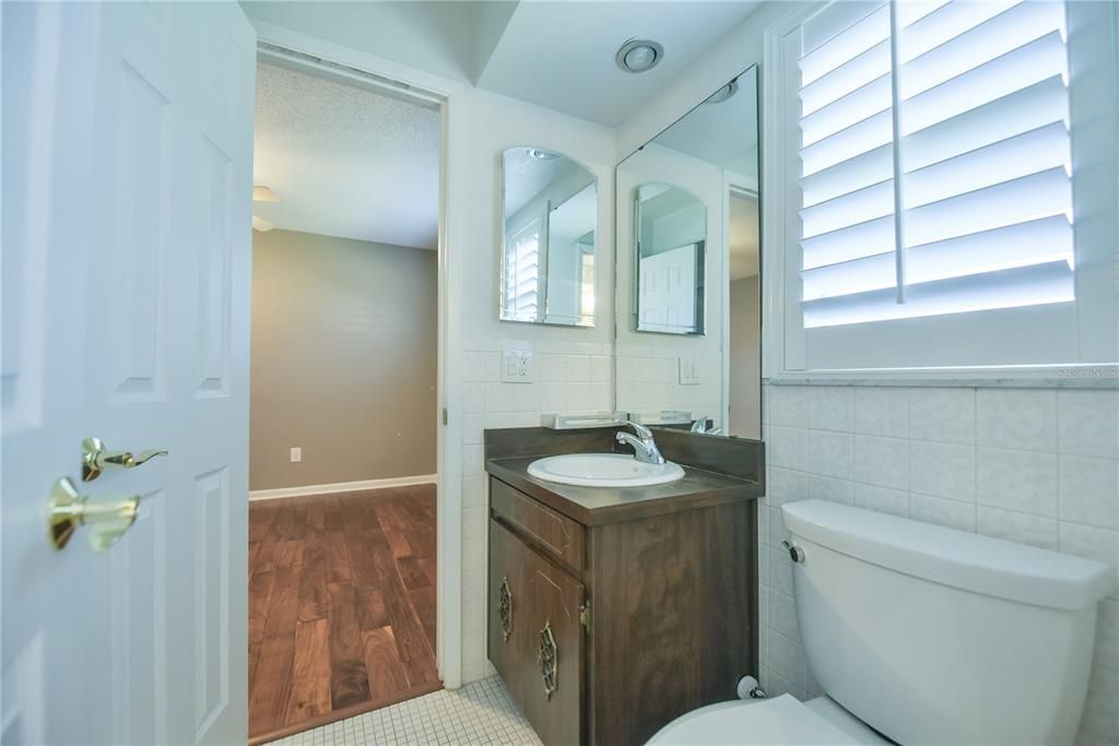 Jack and Jill bathroom has tub with shower, plantation shutter and single sink.